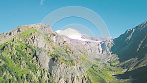 Top view of mountain landscape with snowy peak and green slopes. Clip. Majestic rocky mountains with green forest and