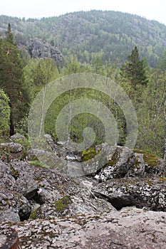 Top view. A mountain river waterfall flows through a river bed through huge boulders with moss