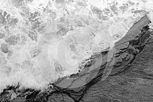 Top view on moving sea water against rocks with waves and foam, texture background pattern in black and white