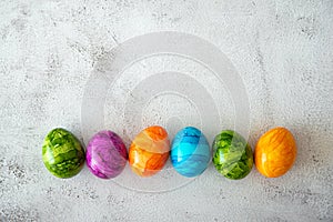 Top view of multicolored colorful Easter eggs in sunlight with shadows over gray textured background.