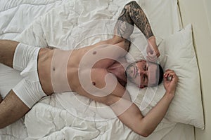 Top view of naked young man on bed. Nude male body. Sexy model laying in big bed. Young muscular male model lying back