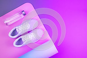 Top view of neon purple and pink colored white sport shoes sneakers, yoga mat, reusable eco glass water bottle.