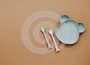 Top view neutral baby tableware on brown background, flat lay