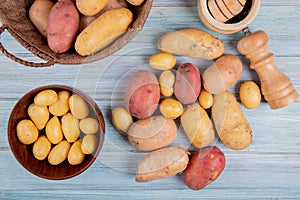 top view of new potatoes in bowl and others of different types in basket with garlic crusher salt and other potatoes on wooden photo