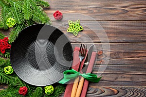 Top view of New Year dinner on festive wooden background. Composition of plate, fork, knife, fir tree and decorations. Merry
