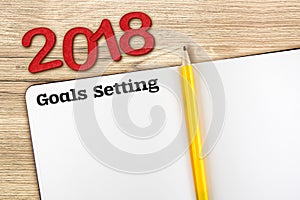 Top view of 2018 new year red number and goals setting with blank open notebook and yellow pencil on wooden table top,Mock up for