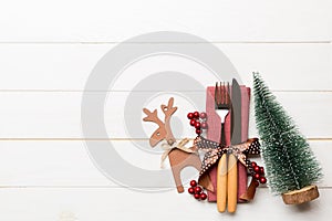 Top view of new year utensils on napkin with holiday decorations and reindeer on wooden background. Christmas dinner concept with