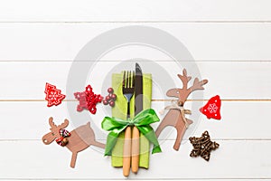 Top view of new year utensils on napkin with holiday decorations and reindeer on wooden background. Christmas dinner concept with