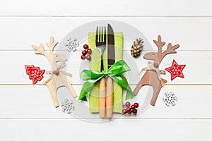 Top view of new year utensils on napkin with holiday decorations and reindeer on wooden background. Close up of christmas dinner