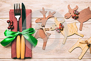 Top view of new year utensils on napkin with holiday decorations and reindeer on wooden background. Close up of christmas dinner