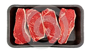 Top view of New York strip steak in a black foam food tray isolated on a white background