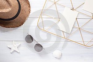 Top view note pad clip frame and summer straw hat with sunglasses on white wood table.summer vacation background