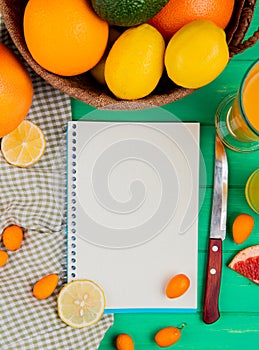 top view of note pad with orange lemon kumquat knife and juice around on green background with copy space