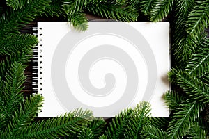 Top view of notebook decorated with a frame made of fir tree on wooden background. New Year time concept