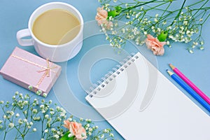 notebook with empty white paper sheet ,colored pencils,coffe with cream cup and floral frame on a pastel blue background