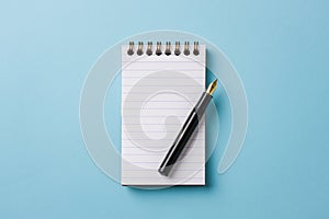 Top view of notebook and fountain pen on blue background