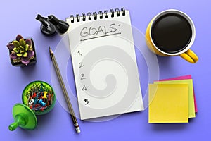 Top view notebook with goals list. Notepad on office table with a cup of coffee, plant, stationery and office supplies. Top view