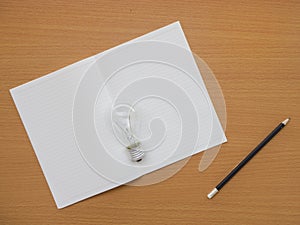 Top view of notebook, light bulb and pencil on wooden table with copy space