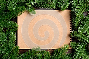 Top view of notebook made of craft paper decorated with a frame made of fir tree on wooden background. New Year time concept