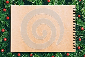 Top view of notebook made of craft paper decorated with a frame made of fir tree on wooden background. New Year time concept