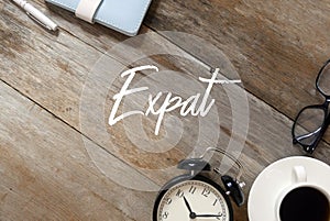 Top view of notebook,pen, clock,a cup of coffee,sunglasses on wooden background written with Expat