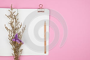 Top view of notebook, pencil and flower on pink background