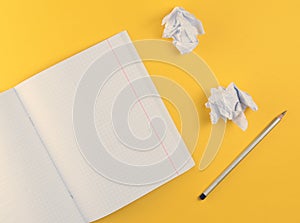 Top view of notebook with pencil and white crumpled paper ball on yellow background. Concept of no idea, education, minimalism.