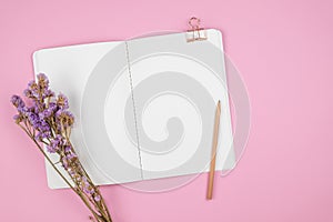 Top view of notebook and violet flower on pink background
