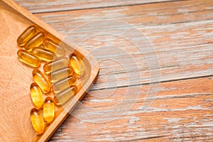 Top view of nutritional supplement gold capsules in wooden plate on wooden table