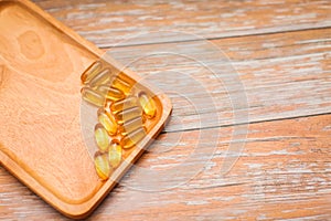 Top view of nutritional supplement gold capsules in wooden plate on wooden table