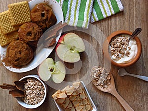 Top view. Oat cereal grain meal, baked and fresh apples, biscuits, yogurt and cinnamon on rustic style oak wood background.