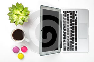 Top view of office desk. Green plant in a pot, cup of coffee, colorful macaroons and modern silver laptop on white background