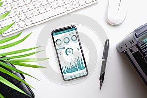 Top view of office desk table with business reports graph chart on mockup smartphone on white desk table. Business management via