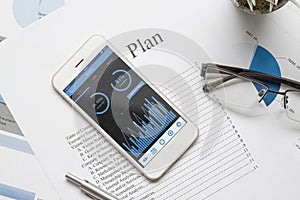 Top view of office desk table with graph chart on mock up smartphone on white desk table. Business management via mobile