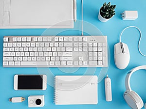 Top view of office desk table with notebook, plastic plant, smartphone and keyboard on blue table background, graphic designer, Cr