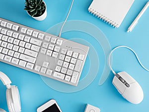 Top view of office desk table with notebook, plastic plant, smartphone and keyboard on blue table background, graphic designer, Cr