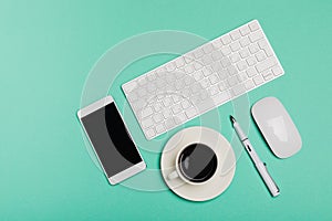 Top view of office desk workspace with smartphone, keyboard, coffee and mouse on blue background with copy space, graphic designer
