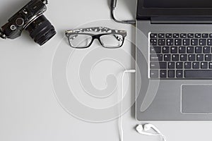 Top view office table concept with camera, laptop notebook, glasses and earphone smartphone on grey table background. Flat lay wi