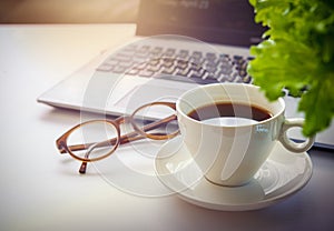 Top view office table desk. Workspace with blank, office supplies, laptop, eyes glasses, green leaf, and hot black coffee cup on w