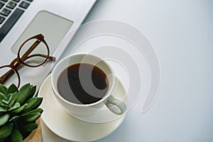 Top view office table desk. Workspace with blank, office supplies, laptop, eyes glasses, green leaf, and hot black coffee cup on w