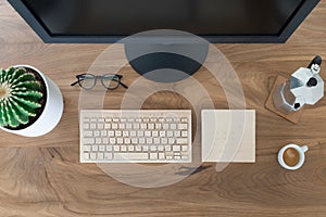 Top view office table desk. Workspace with large monitor screen, a wooden keyboard, a trackpad, a cactus, glasses, a coffee cup photo