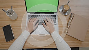 Top view on the office table with a laptop computer with green screen and female hands typing on a keyboard. Glasses