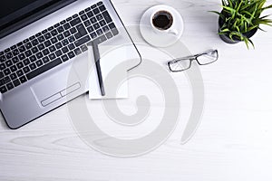 Top view of office work space, wooden desk table with laptop notebook,keyboard ,pen,eyeglasses,phone,notebook and cup of coffee.