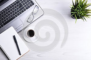 Top view of office work space, wooden desk table with laptop notebook,keyboard ,pen,eyeglasses,phone,notebook and cup of coffee.