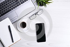 Top view of office work space, wooden desk table with laptop notebook,keyboard ,pen,eyeglasses,phone,notebook and cup of coffee.