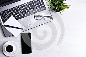 Top view of office work space, wooden desk table with laptop notebook,keyboard ,pen,eyeglasses,phone,notebook and cup of coffee.