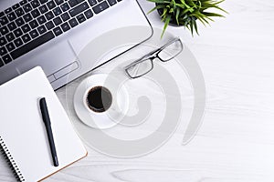 Top view of office work space, wooden desk table with laptop notebook,keyboard ,pen,eyeglasses,phone,notebook and cup of coffee.