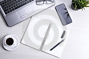 Top view of office work space, wooden desk table with laptop notebook,keyboard ,pen,eyeglasses,phone,notebook and cup of coffee.