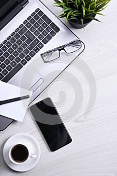 Top view of office work space, wooden desk table with laptop notebook,keyboard ,pen,eyeglasses,phone,notebook and cup of coffee.