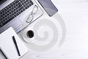 Top view of office work space, wooden desk table with laptop notebook,keyboard ,pen,eyeglasses,phone,notebook and cup of coffee.